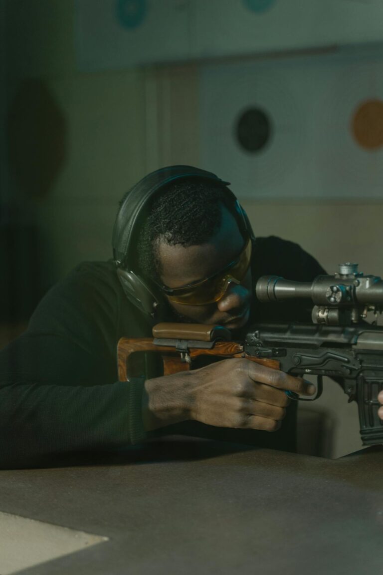 A man aiming a rifle with precision in an indoor shooting range, showcasing shooting skill and safety equipment.