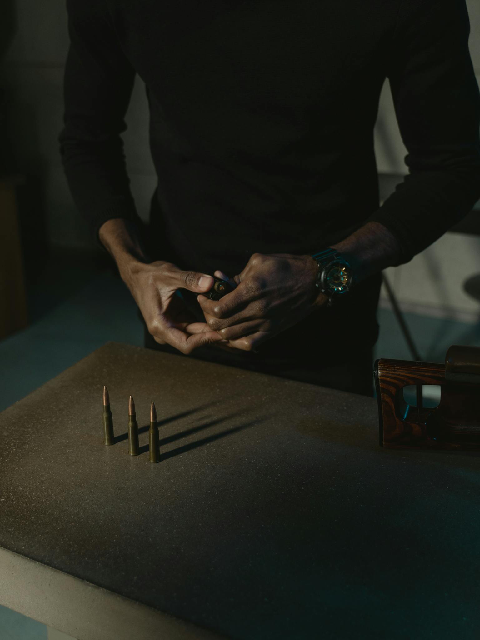 Close-up of a person handling rifle ammunition indoors, emphasizing firearms and security theme.