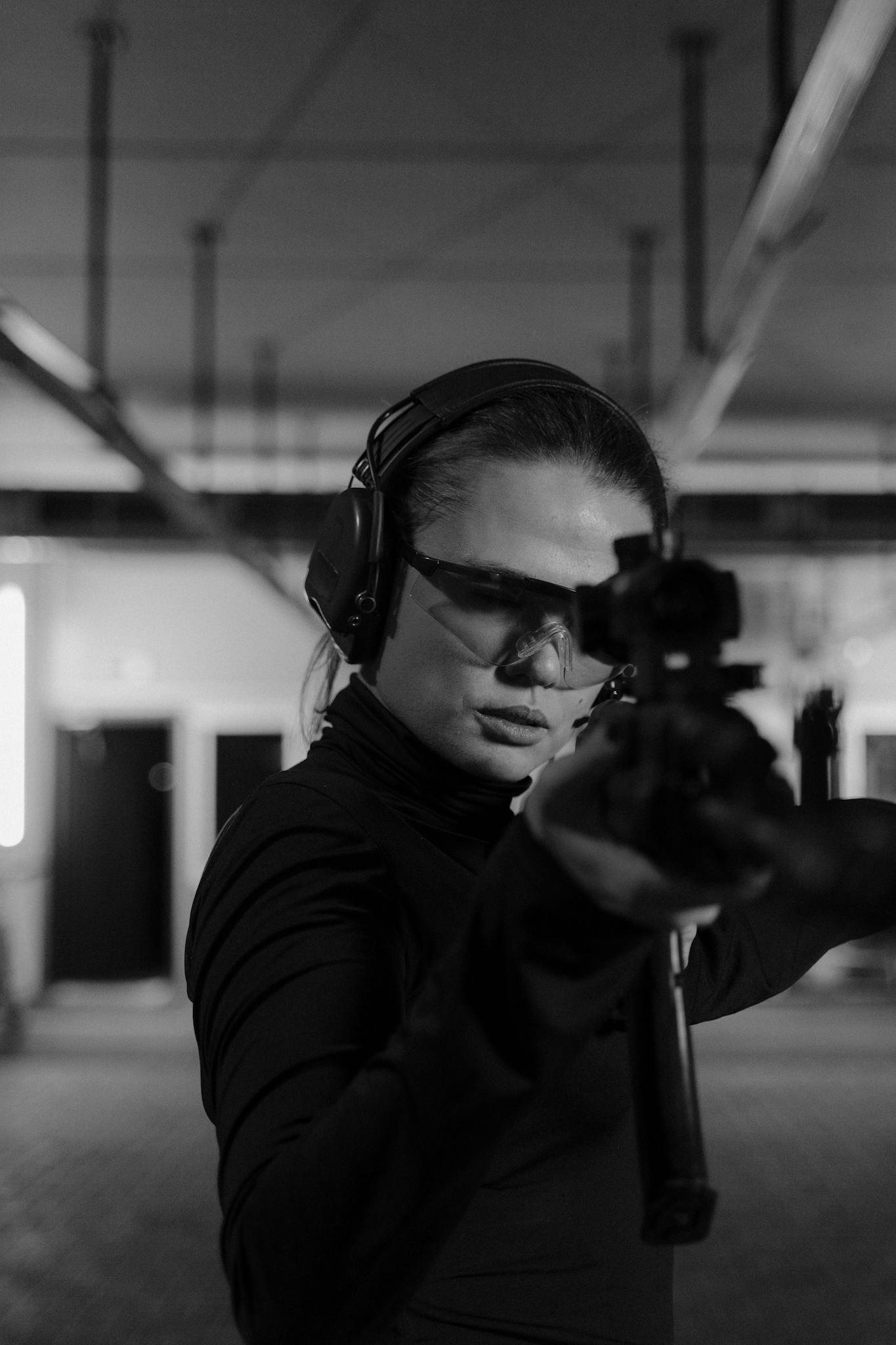 Woman in protective gear aiming a rifle at an indoor shooting range.